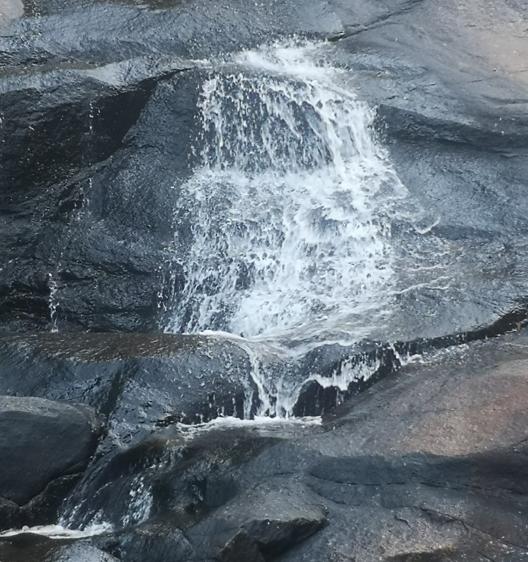 Water flowing over the smooth dark rock of one of the seven pools at Telaga Tujuh, Langkawi