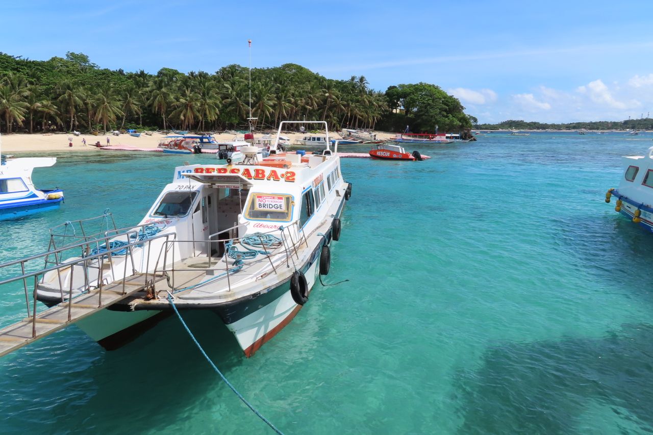 Tour boats moored off a palm-backed island beach in clear turquoise water, evocative of a Langkawi island stop
