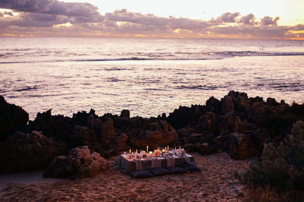 Candlelit private dinner table set on a beach at sunset, evocative of a Langkawi honeymoon