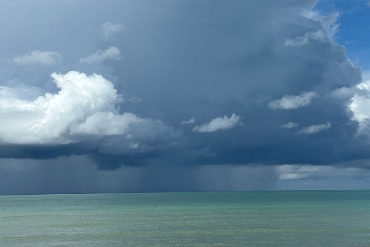 A rain squall and monsoon clouds over a turquoise tropical sea, evocative of Langkawi in August