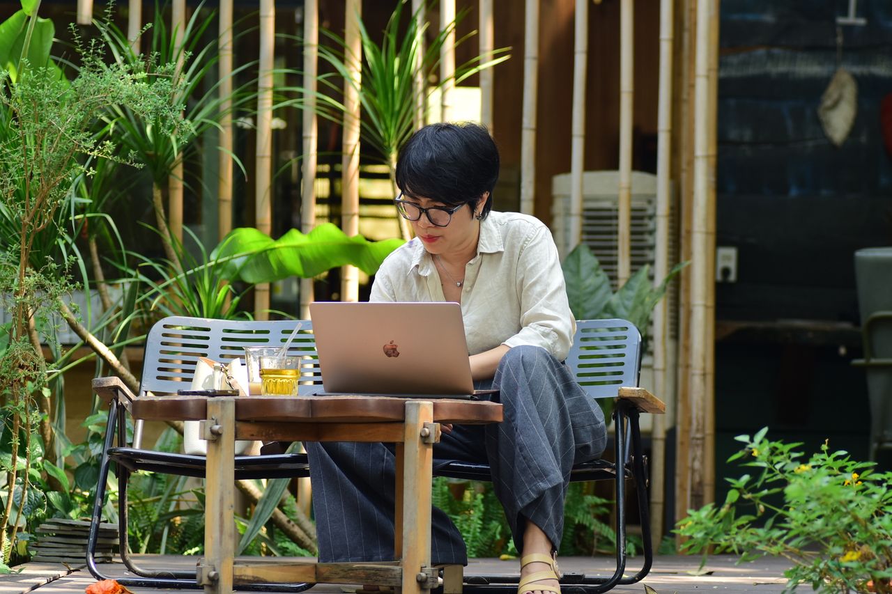 A remote worker using a laptop at an outdoor garden cafe surrounded by bamboo and tropical plants