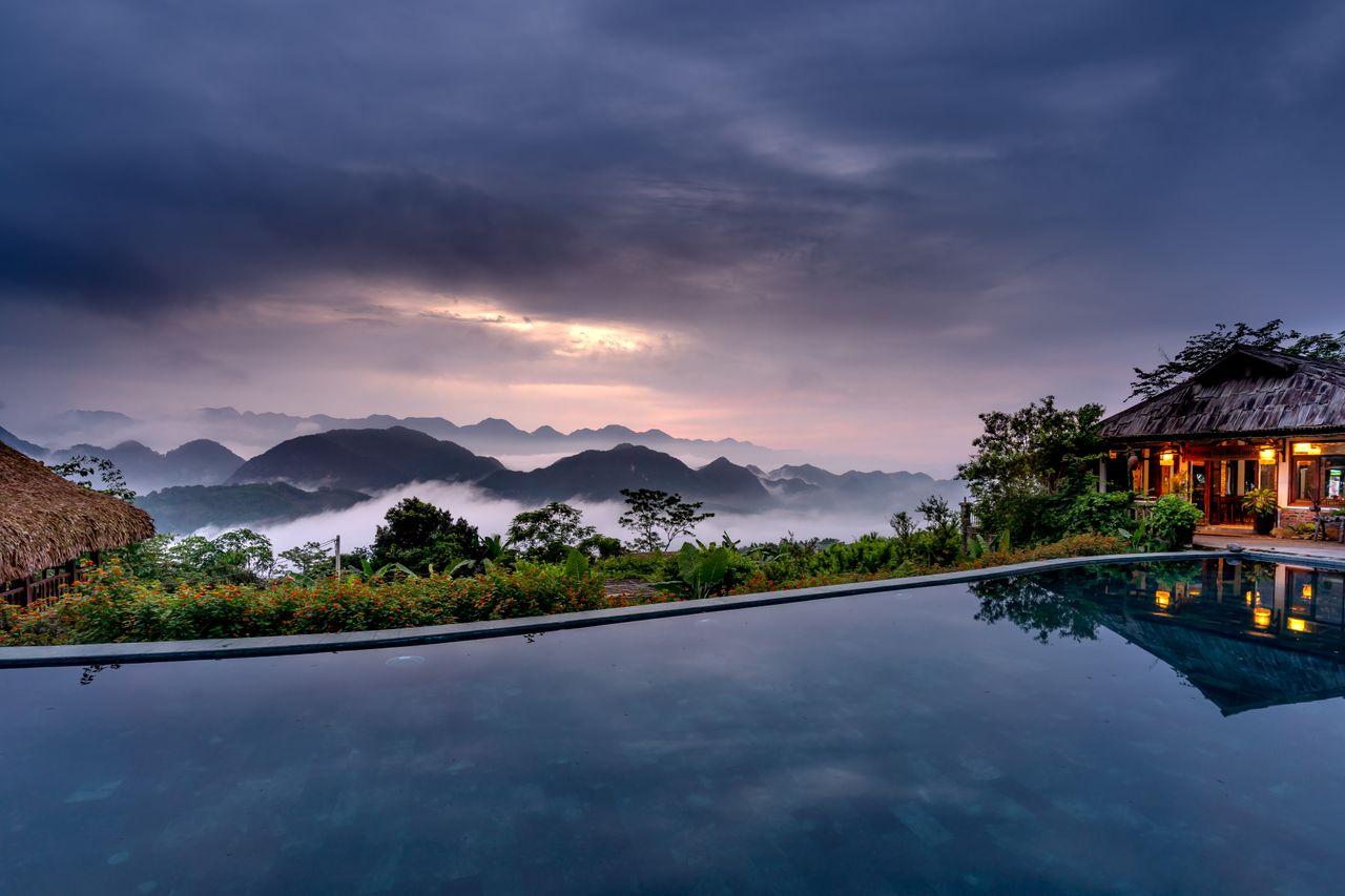 A tropical infinity pool and resort overlooking misty mountains under moody monsoon clouds, evocative of Langkawi in September