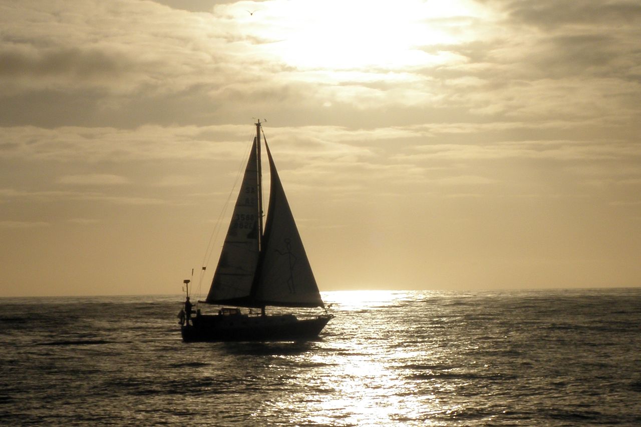 Sailboat silhouetted against a golden sunset over calm sea, evocative of a Langkawi sunset cruise