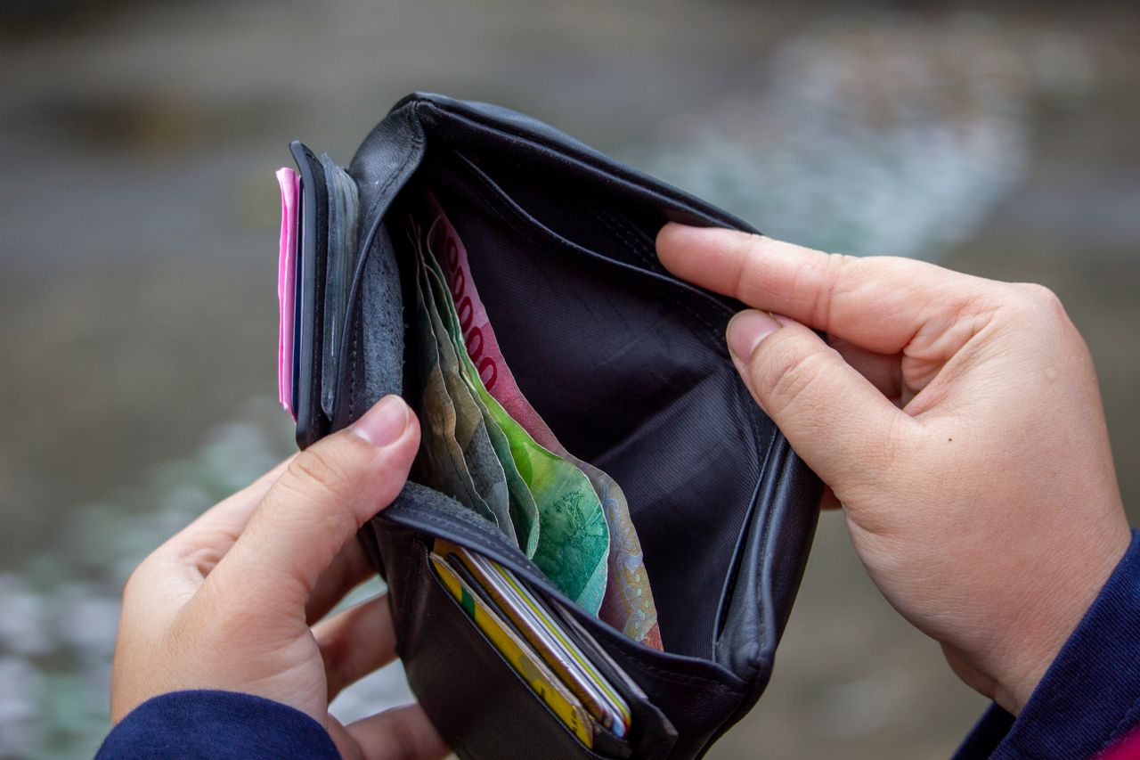 A person holding an open wallet with banknotes outdoors, evocative of budgeting on the go