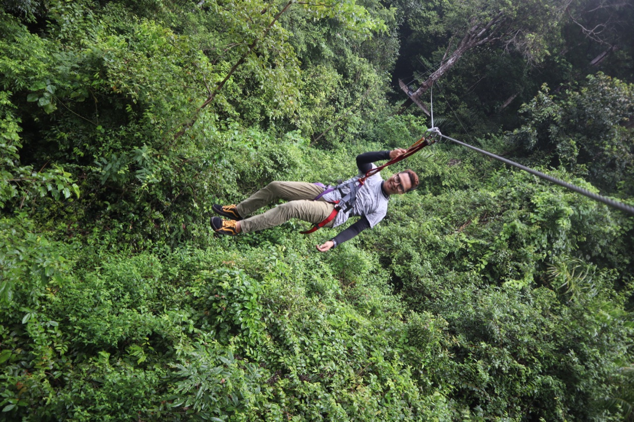 A harnessed visitor riding a flying fox zip line across the green forest canopy at SKYTREX Langkawi